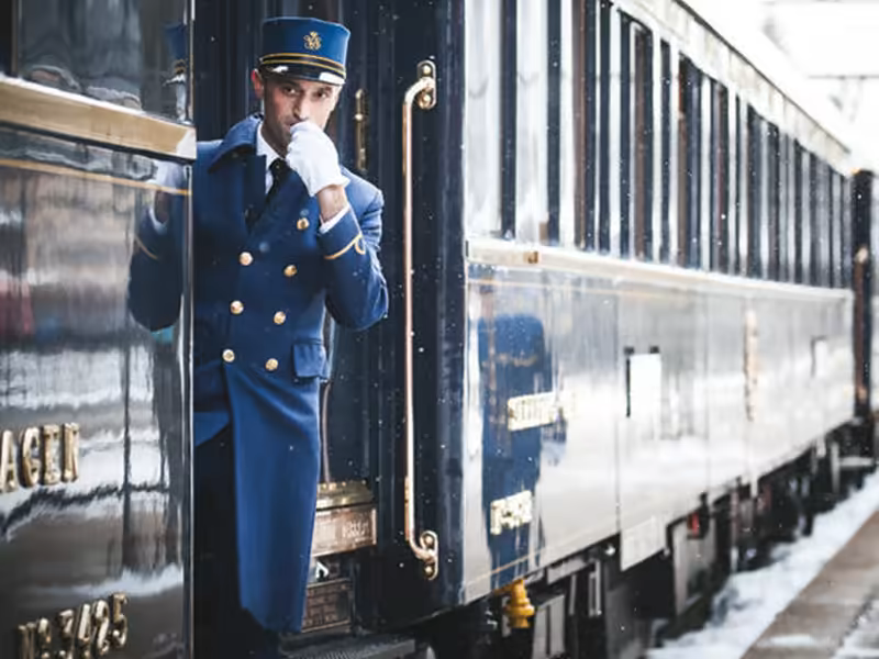 A Venice Simplon-Orient-Express steward in blue livery at the door of a carriage